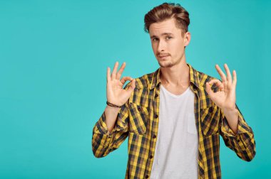 Genç adam OK işareti, mavi arka plan, duygu gösteriyor. Yüz ifadesi, stüdyoda kameraya bakan erkek, duygusal konsept, olumlu duygular.