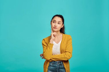 Gizemli, sevimli bir kadın, mavi arka plan, olumlu duygu. Yüz ifadesi, stüdyoda kameraya bakan kadın, duygusal konsept, duygular.