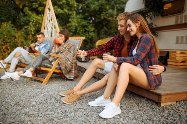 Mutlu arkadaşlar ormanda piknik yaparken selfie çekerler. Gençler karavanda yaz macerası yaşıyor, arka planda kamp arabası. Karavanla seyahat eden iki çift.