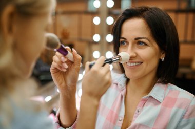 Anne ve kızı makyaj salonunda fırça kullanıyor. Anne ve küçük kız birlikte oyun stilistleri, mutlu çocukluk, büyüleyici aile.