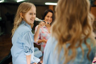 Anne ve kızı makyaj salonunda toz kullanıyor. Anne ve küçük kız birlikte oyun stilistleri, mutlu çocukluk, büyüleyici aile.