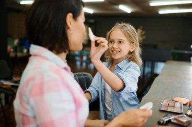 Salonda annesine makyaj yapan bir kız çocuğu. Anne ve küçük kız birlikte oyun stilistleri, mutlu çocukluk, büyüleyici aile.