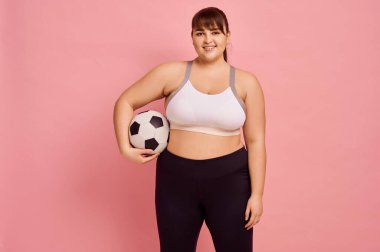 Futbol topu gibi şişman bir kadın, pembe arka plan, vücut pozitifliği. Obezite savaşı, sağlıklı bir yaşam tarzı için mücadele