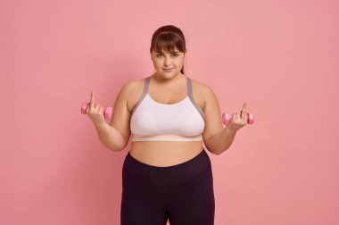 Şişman kadın uygunsuz bir jest yapıyor, pembe arka plan, vücut pozitifliği. Obezite savaşı, sağlıklı bir yaşam tarzı için mücadele