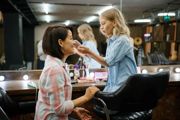 Mother and daughter do their makeup in salon. Mom and little girl play hairdressers together, happy childhood, glamour family