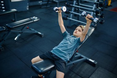 Spor salonundaki halterlerle egzersiz yapan bir çocuk. Spor kulübünde eğitim gören genç, sağlık hizmetleri ve sağlıklı yaşam tarzı, spor yapan okul çocuğu.