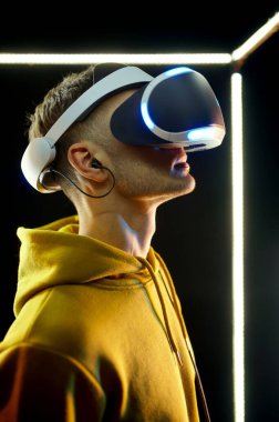 Genç oyuncu oyunu sanal gerçeklik miğferi ve parlayan küp içinde oyun sahası kullanarak oynar. Koyu renk kulüp iç mekanı, arka planda spot ışığı, VR teknolojisi ve 3 boyutlu vizyonu var.