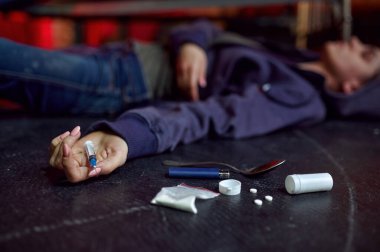 Uyuşturucu bağımlısı bir kadın çalışma odasında yerde yatıyor. Arka planda, aşırı dozdan ölmüş. Uyuşturucu bağımlılığı sorunu, bağımlı insanların sonsuz depresyonu.