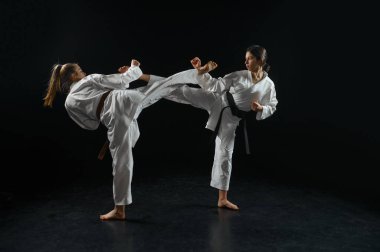 İki kadın karate dövüşçüsü, çarpışma halinde, beyaz kimono, siyah dumanlı arka plan. Karateka antreman, dövüş sanatları, dövüş yarışması