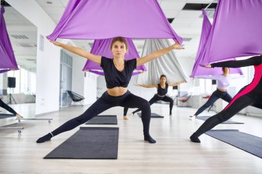 Sinek yogası, hamaklı kadın grup eğitimi. Fitness, pilates ve dans egzersizleri karışımı. Kadınlar spor stüdyosunda yoga yapıyor.
