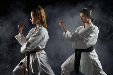 Kadın karatekalar, beyaz kimono eğitimi, çarpışma duruşu, karanlık bir altyapı. Antrenman yapan karate dövüşçüleri, dövüş sanatları, dövüşen kadınlar