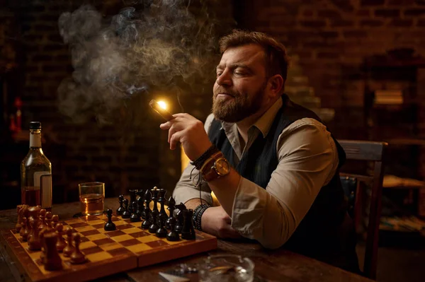 男は背景に葉巻 ドリンクアルコール飲料を吸うとチェス 本棚やヴィンテージオフィスのインテリアを再生します タバコの喫煙文化 特定の味 男性喫煙者レジャーでザチェスボード — ストック写真