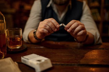 Adam sigarayı, kötü alışkanlığı ve bağımlılığı bırakıyor. Masada alkollü içecek, arka planda klasik ofis içkisi. Tütün içme kültürü, spesifik lezzet