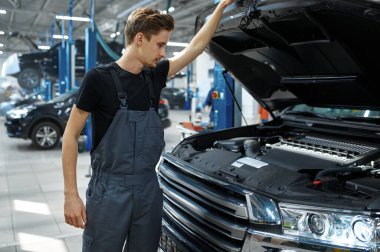 Açık kaputta erkek tamirci, alt manzara, araba servisi. Araç tamirhanesi, üniformalı adam, arka planda otomobil istasyonu.