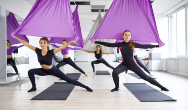 Sinek yogası, hamaklı kadın grup eğitimi. Fitness, pilates ve dans egzersizleri karışımı. Kadınlar spor stüdyosunda yoga yapıyor.
