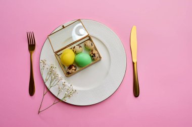 Paskalya yumurtaları tabakta ve sofra takımı pembe arka planda. Bahar ağacı çiçeği ve paskalya yemeği, bayram kutlaması için taze çiçek süsü, etkinlik sembolü.