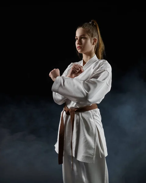 female karate fighter in white kimono, welcome sign, dark background. Karateka on workout, martial arts, training before fighting competition