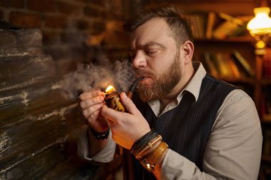 Sakallı adamın portresi pipoyu kibritle yakıyor, yakından bakıyor. Tütün içme kültürü, zengin bir tat. Erkek içicilerin boş vakitleri ofiste