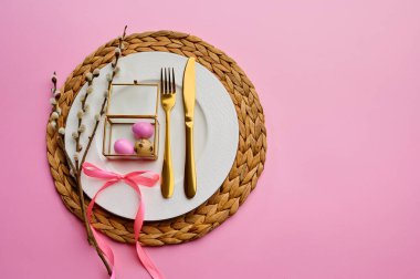 Çiçekli söğüt, tabakta Paskalya yumurtası ve pembe arka planda sofra takımı. Bahar ağacı çiçeği ve paskalya yemeği, bayram kutlaması için taze çiçek süsü, etkinlik sembolü.