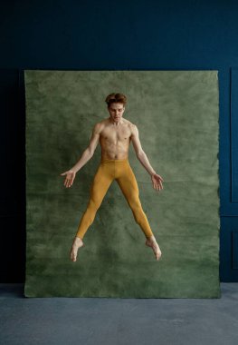 Erkek balerin dans stüdyosunda zıplıyor, arka planda grunge duvar var. Kaslı vücutlu, zarif ve zarif bir sanatçı.