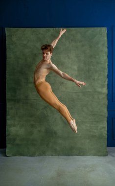 Erkek balerin dans stüdyosunda zıplıyor, arka planda grunge duvar var. Kaslı vücutlu, zarif ve zarif bir sanatçı.