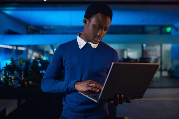 一位经理在夜间工作在笔记本电脑上 男性工人 背景为深色商业中心内部 现代工作场所 — 图库照片