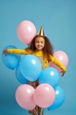 Şapkalı küçük kız elinde bir sürü balon tutuyor.