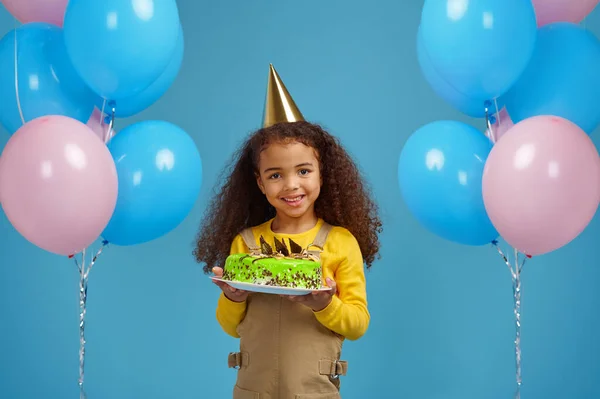 Забавная маленькая девочка в кепке держит торт на день рождения — стоковое фото
