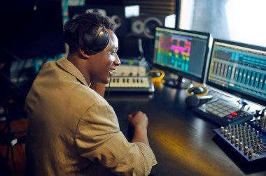 Kulaklıklı mutlu erkek DJ, arka planda stüdyo iç mekan kaydı yapıyor. Sentezleyici ve ses karıştırıcı, müzisyen işyeri, yaratıcı süreç