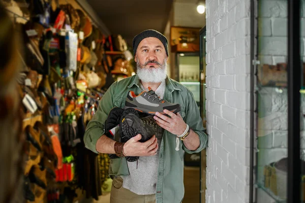 Бородатый охотник выбирает сапоги в оружейном магазине — стоковое фото