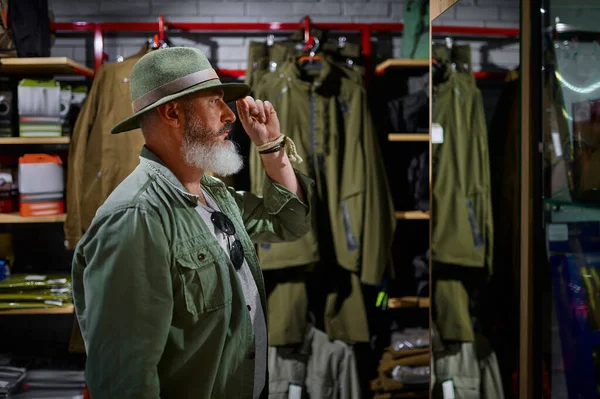 Baard mannelijke jager kiezen hoed in pistool winkel — Stockfoto