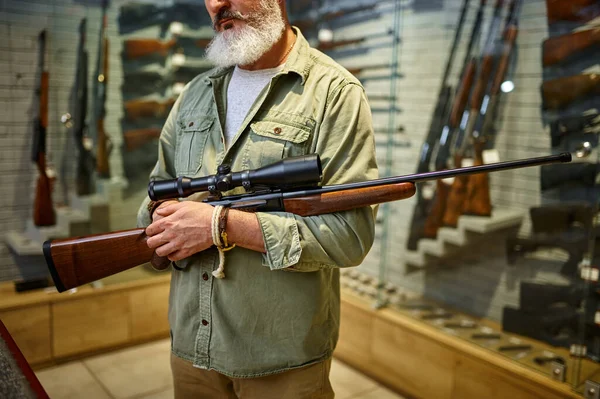 Hunter sostiene rifle con mira óptica en la tienda de armas —  Fotos de Stock