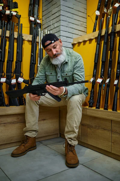 Sakallı adam otomatik tüfeği silah dükkanında seçiyor. — Stok fotoğraf