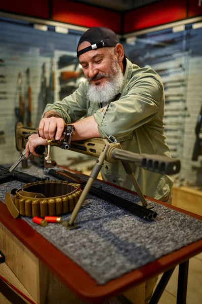 Een man met baard poseert bij een krachtig geweer in de wapenwinkel. — Stockfoto