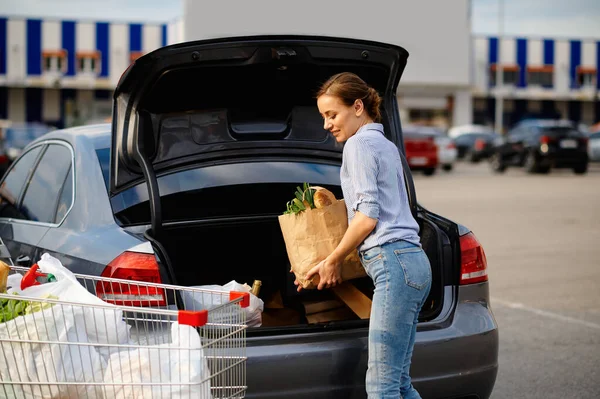 Woman with cart puts her purchases in car trunk — Stock Photo, Image