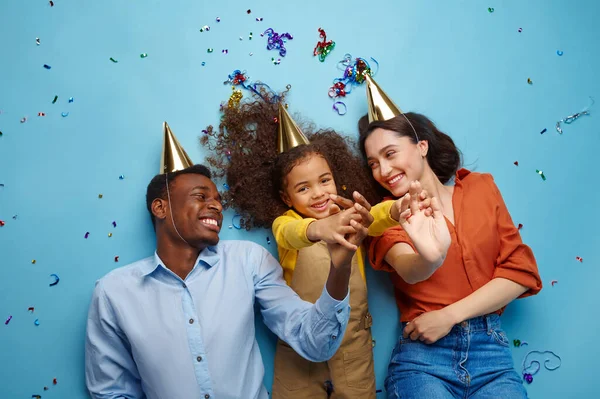 戴着帽子的有趣家庭庆祝生日 蓝色背景 漂亮的小女孩和她的父母 庆祝活动 气球和糖果装饰 — 图库照片