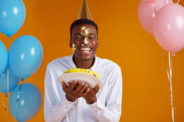 戴着帽子的快乐男人用生日蛋糕 黄色背景涂了他的脸 笑的男人得到了惊喜 庆祝活动 气球装饰 — 图库照片