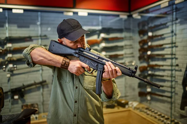 Man verkoper houdt automatisch geweer in de wapenwinkel — Stockfoto