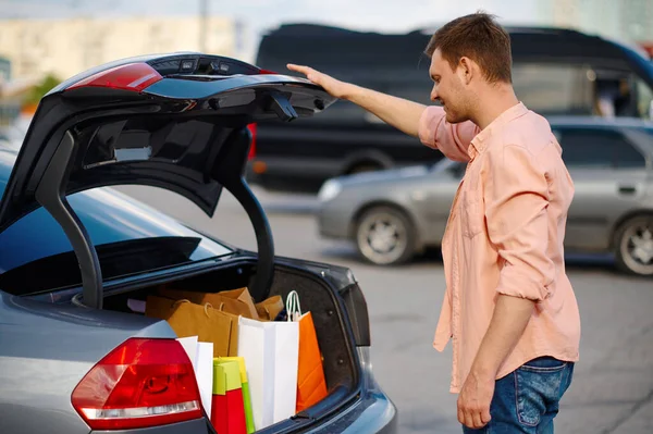 El hombre pone sus compras en el maletero en el estacionamiento —  Fotos de Stock