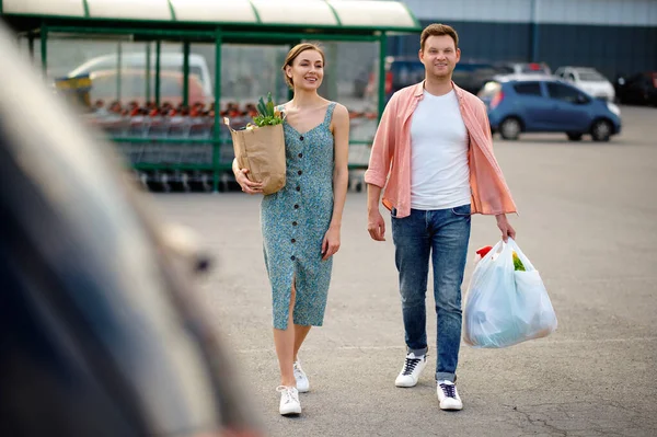 Mladý pár s taškami na parkování v supermarketu — Stock fotografie
