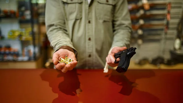 Hombre sostiene pistola y balas en la tienda de armas —  Fotos de Stock