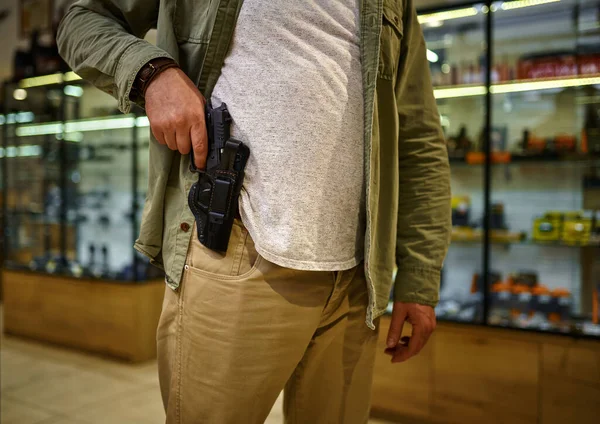 Een man trekt een pistool uit een holster in een wapenwinkel. — Stockfoto