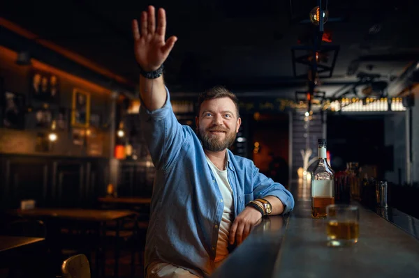 Γενειοφόρος άνδρας με σηκωμένο χέρι κάθεται στο μπαρ — Φωτογραφία Αρχείου