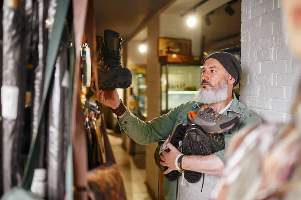 Sakallı erkek avcı silah dükkanında çizme seçiyor. — Stok fotoğraf