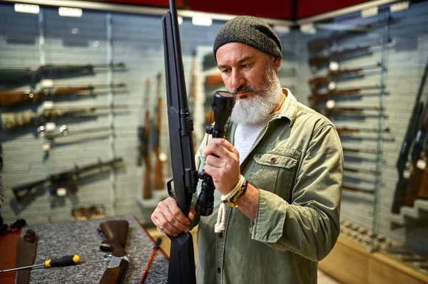 Bearded hunter buying optical sight in gun store — Zdjęcie stockowe