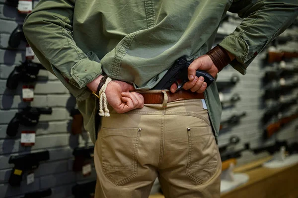 Man puts the pistol in his belt in gun store — Zdjęcie stockowe