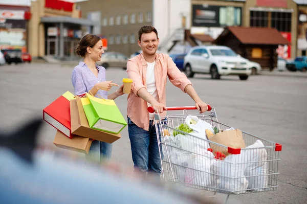 Family couple with bags in cart on car parking — Stock Photo, Image