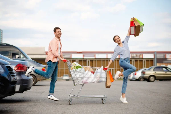 Fröhliches Familienpaar mit Wagen auf Parkplatz — Stockfoto