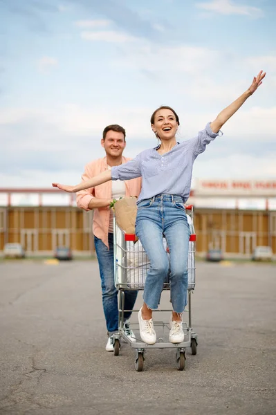 Family couple rides in cart on supermarket parking — Foto de Stock