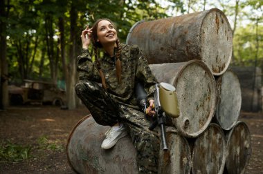 Paintball silahı olan bir savaşçı paslı fıçılarda poz verir.